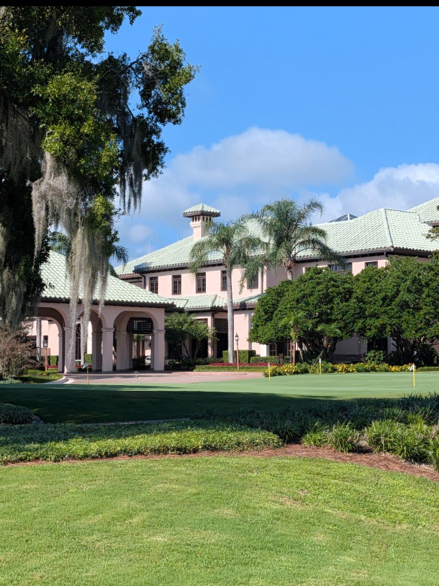 Clubhouse with a restored green tile roof beside manicured Florida grounds